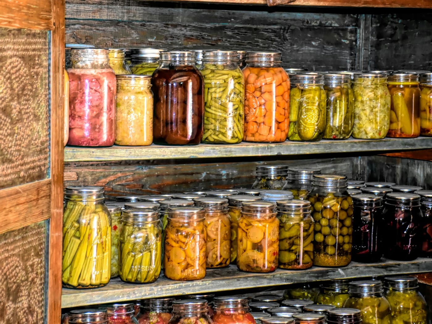 Shelves of home-preserved jars — beans, carrots, pickles — on weathered wooden racks.